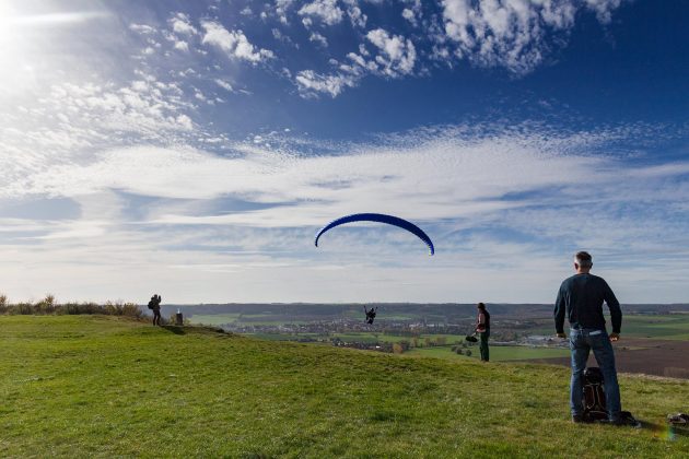 Ein Paraglider startet am Hang während auf dem Fluplatz Laucha die Segelflieger landen.